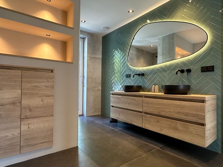 Groene visgraat tegels achter dubbele wastafel met zwarte kranen en houtlook meubel, badkamerinspiratie